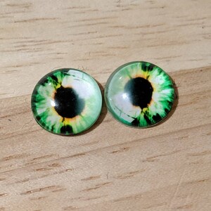 May include: Two green glass eyes with black pupils and yellow irises. The eyes are round and have a glossy finish.