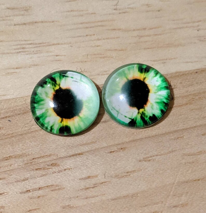 May include: Two green glass eyes with black pupils and yellow irises. The eyes are round and have a glossy finish.
