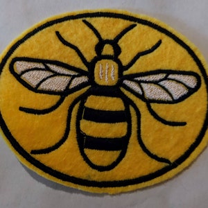May include: A yellow embroidered patch with a black outline depicting a bee with black and yellow stripes. The bee has white wings and is centred on the patch.