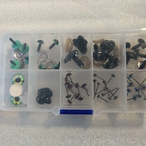May include: A clear plastic storage box with multiple compartments filled with various sizes and colors of plastic safety eyes for crafts. The box has a blue handle.