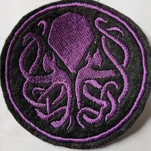 May include: Purple embroidered patch featuring a stylised octopus design on a black background. The octopus is within a circle with a purple outline.