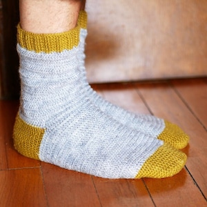 Peut inclure: Une paire de chaussettes en crochet grises et jaunes. Les chaussettes ont un motif côtelé et un revers jaune.