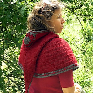 Puede incluir: Una bufanda de ganchillo roja con ribetes grises. La bufanda la lleva puesta una persona de pie en un bosque.