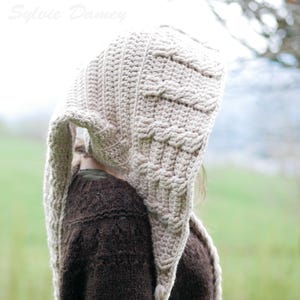 Peut inclure: Un bonnet à capuche en crochet beige avec une longue écharpe fluide. Le bonnet présente un design unique avec un motif tressé.