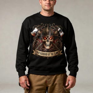 May include: Black sweatshirt with a detailed graphic of a skull in a firefighter's helmet, glowing red eyes, and crossed axes. The banner below reads "BROTHERHOOD OF THE FLAME". The design is intricate and colourful.