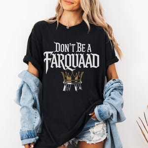 May include: Black t-shirt with the text "DON'T BE A FARQUAAD" in white, stylized font, and a gold crown graphic. The shirt is worn with a light blue denim jacket and denim shorts.