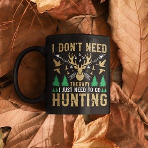 Puede incluir: Taza de café negra con un diseño blanco que dice "No necesito terapia, solo necesito ir de caza". El diseño también incluye una cabeza de ciervo con cuernos y una escena de bosque.