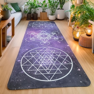 May include: A purple yoga mat with a white geometric design of a flower of life, a metatron's cube, and a sacred geometry pattern. The mat is on a wooden floor.