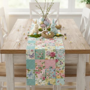 May include: A wooden table is set for Easter with a floral patchwork table runner. Decorative elements include two bunny figurines, a glass vase with eggs, and small nests with eggs. The runner features butterflies and flowers.