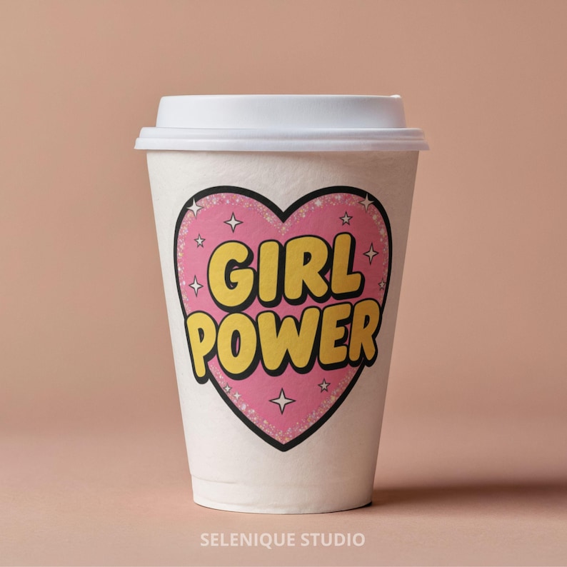 Op de afbeelding: Een witte papieren koffiebeker met een wit deksel. De beker heeft een roze hart met de woorden "GIRL POWER" in het geel, omlijnd in zwart. Het hartontwerp bevat kleine steraccenten. De woorden "SELENIQUE STUDIO" staan onderaan.