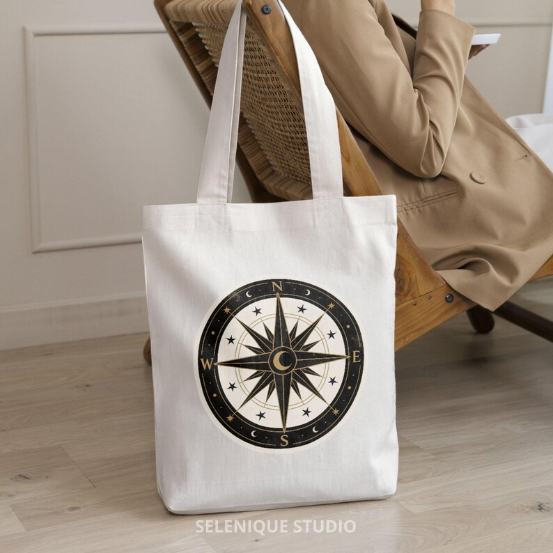 Pu&ograve; includere: Borsa tote bianca con un design a bussola nero e oro. La rosa dei venti &egrave; circondata da stelle e lune crescenti. La borsa ha manici lunghi e il testo "SELENIQUE STUDIO" in basso.