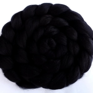 May include: A black wool roving, a type of fibre used for spinning yarn, is shown in a circular shape. The roving is tightly packed and has a soft, fluffy texture.