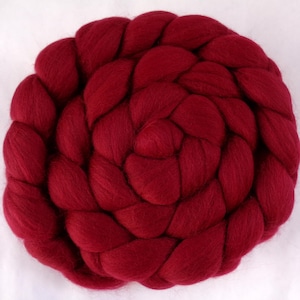 Könnte beinhalten: Nahaufnahme einer tief roten Wollroving, die zu einer kreisförmigen Form geflochten ist. Die Roving ist weich und flauschig, und der Zopf ist fest geflochten.
