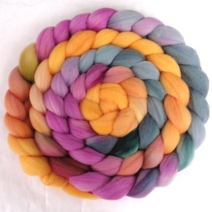 May include: A circular arrangement of colorful wool roving in shades of orange, pink, purple, and teal. The wool is braided in a spiral pattern, creating a textured, handcrafted appearance. The colors blend together, creating a vibrant and artistic display.