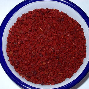 Könnte beinhalten: Eine weiße Schüssel mit blauem Rand, gefüllt mit einer großen Menge kleiner, leuchtend roter Annatto-Samen.