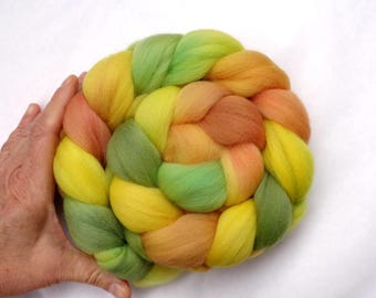 May include: A braid of colorful wool roving in shades of green, yellow, and orange. The roving is arranged in a circular shape and is ready for felting.