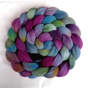 Può includere: Uno stoppino di lana spesso e intrecciato, disposto in una spirale circolare. La fibra presenta una tavolozza di colori variegati che include sfumature di magenta intenso, verde acqua brillante, verde salvia tenue e blu ardesia spento.