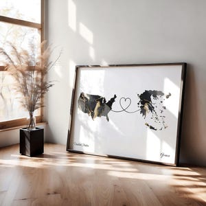 Framed map print leaning on a wooden floor against a white wall next to a tall glass vase filled with dried grasses.