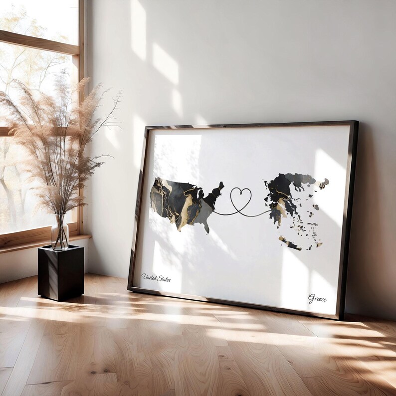 Framed map print leaning on a wooden floor against a white wall next to a tall glass vase filled with dried grasses.