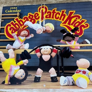 May include: A 1986 Cabbage Patch Kids calendar featuring six dolls in a gym setting. One doll hangs from rings, one does a handstand, one lifts a barbell, and others sit or pose. The text reads 1986 Calendar and Cabbage Patch Kids in yellow.