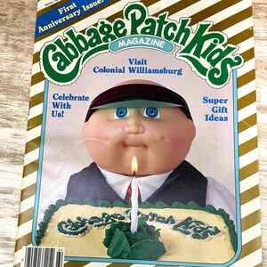 May include: A Winter 1986 Cabbage Patch Kids Magazine featuring a doll wearing a dark visor and vest behind a cake with a single lit candle. The cover text includes First Anniversary Issue, Visit Colonial Williamsburg, Celebrate With Us, and Super Gift Ideas.