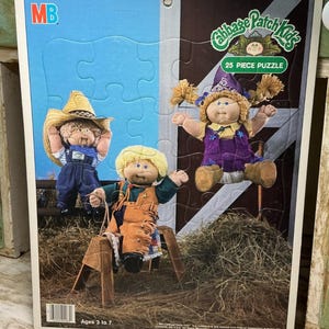 May include: A 25-piece Cabbage Patch Kids jigsaw puzzle featuring three dolls in western-themed outfits. One doll wears a straw hat and denim overalls, another wears a purple hat and outfit, and the third sits on a wooden horse in a barn setting.
