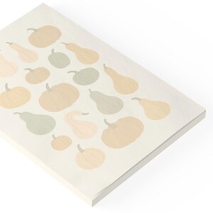 May include: A rectangular, off-white decorative board featuring a pattern of various gourds in shades of beige, peach, and green. The gourds are arranged in a repeating design, creating a fall or harvest theme. The board is angled, showing its thickness.