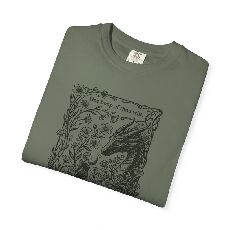 May include: An olive green t-shirt featuring a black ink-style graphic of a dragon and a person surrounded by flowers. The text above the dragon reads, One boop, if thou wilt. The shirt has a crew neckline and a visible size L tag at the collar.