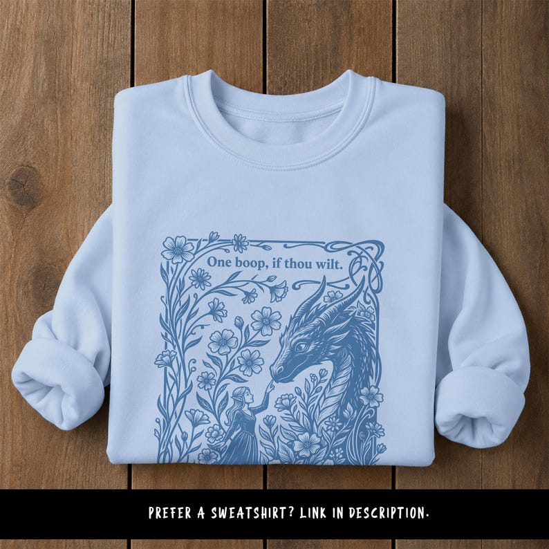 May include: A light blue crewneck sweatshirt featuring a dark blue graphic print of a person touching a dragon's nose amidst flowers. The text "One boop, if thou wilt." is printed above the dragon. The bottom text reads "PREFER A SWEATSHIRT? LINK IN DESCRIPTION."