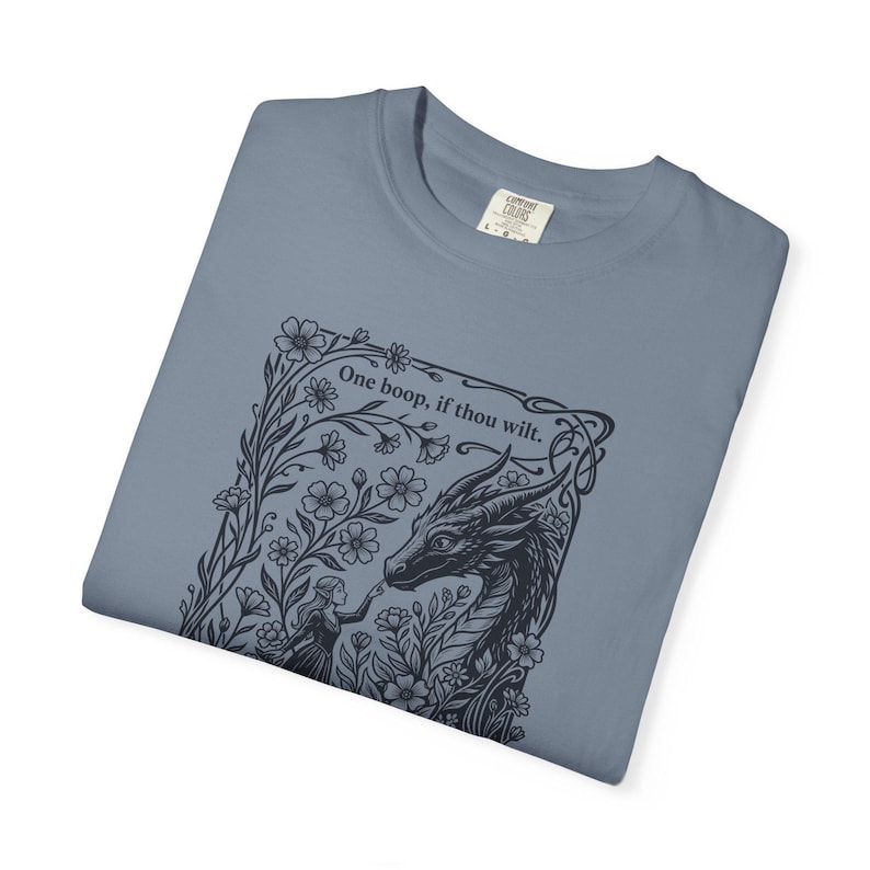 May include: A slate blue t-shirt featuring a dark navy graphic print of a dragon and a person touching noses amidst flowers. The text "One boop, if thou wilt." is printed above the dragon. The shirt has a Comfort Colors brand label at the neck.