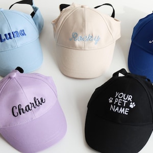 May include: Five baseball caps in light blue, beige, royal blue, lavender, and black. Each cap is embroidered with a name: Luna, Rocky, Max, Charlie, and Your Pet Name. The caps have ear holes and adjustable straps for pets.