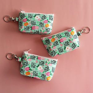 May include: Three small zippered pouches with a floral print and the text "I Don't Like You Either" repeated on each pouch. The pouches are attached to silver key rings.