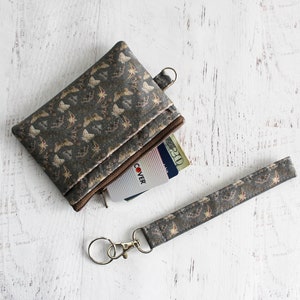 May include: A small zippered pouch with a brown and gold butterfly print. The pouch is open and a credit card is visible inside. A matching lanyard with a key ring is also included.
