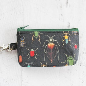 May include: A small black zippered pouch with a green zipper and a silver key ring. The pouch is printed with a pattern of colorful beetles.