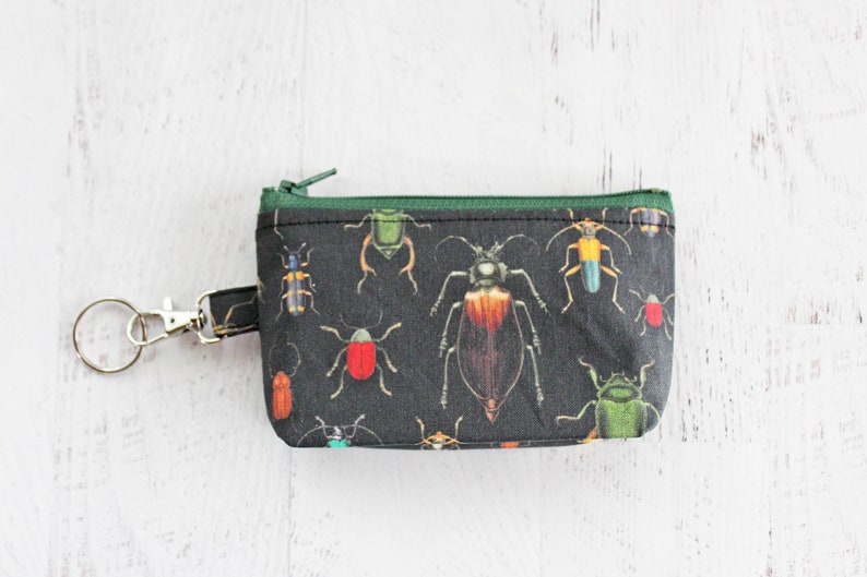 May include: A small black zippered pouch with a green zipper and a silver key ring. The pouch is printed with a pattern of colorful beetles.