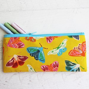 May include: A yellow pencil case with a zipper closure and a colorful butterfly print. The case is filled with three pens.