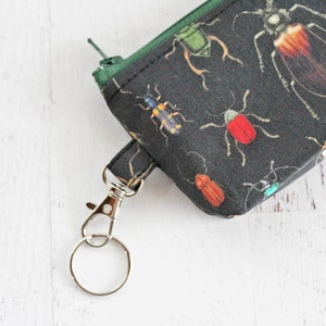 May include: A black fabric zippered pouch with a green zipper pull and a silver key ring. The pouch is decorated with a repeating pattern of colorful insects.