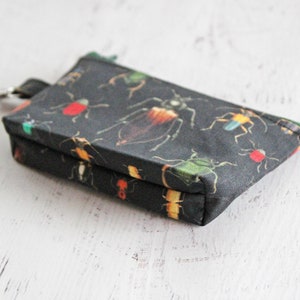 May include: A small black zippered pouch with a key ring. The pouch is decorated with a pattern of colorful insects.