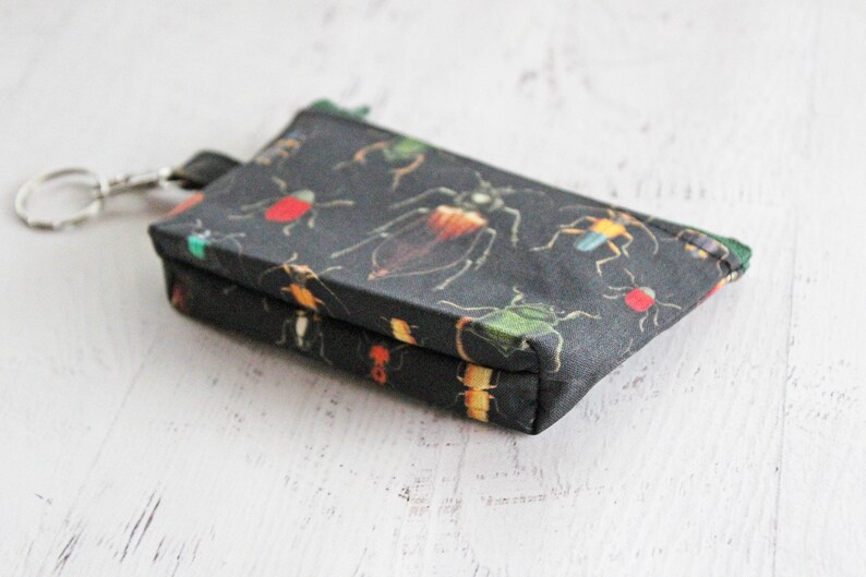 May include: A small black zippered pouch with a key ring. The pouch is decorated with a pattern of colorful insects.