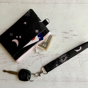 Cartera de muñeca vintage con portadocumentos, diseño de luna y estrellas atómicas, con estampado rosa y negro de inspiración de mediados de siglo.