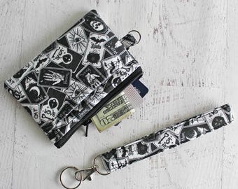 May include: A black and white fabric wallet and matching keychain. The wallet is zippered and contains cash and cards. Both items feature a repeating pattern of occult symbols and text, including "Love" and "Spells".