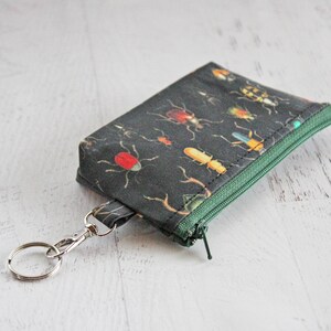 May include: A small black zippered pouch with a key ring. The pouch is decorated with a pattern of colorful insects on a dark background.