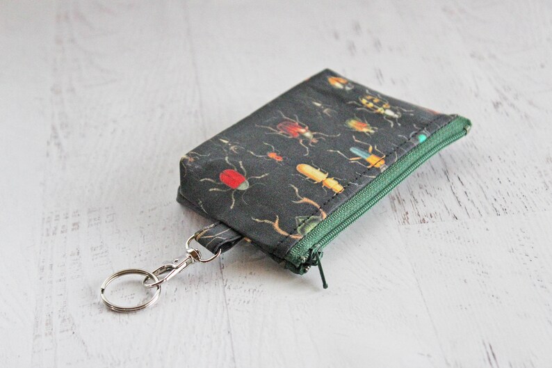 May include: A small black zippered pouch with a key ring. The pouch is decorated with a pattern of colorful insects on a dark background.