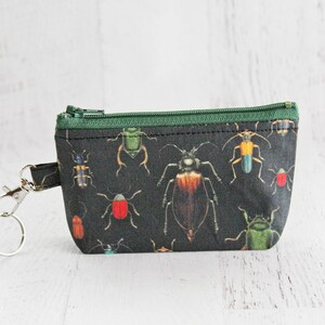 May include: A small black zippered pouch with a green zipper and a key ring. The pouch is printed with a pattern of colorful beetles.