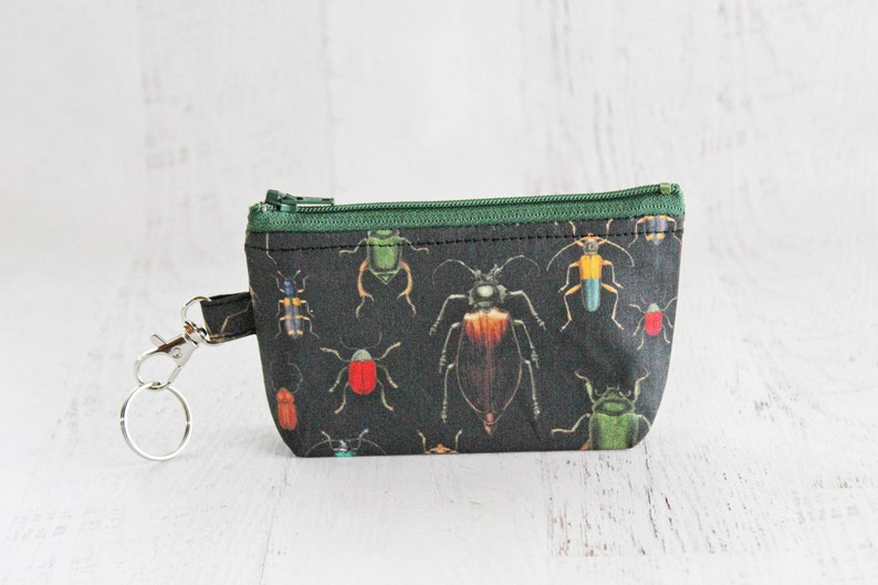May include: A small black zippered pouch with a green zipper and a key ring. The pouch is printed with a pattern of colorful beetles.