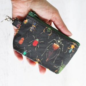 May include: A small black zippered pouch with a key ring. The pouch is covered in a pattern of colorful beetles.