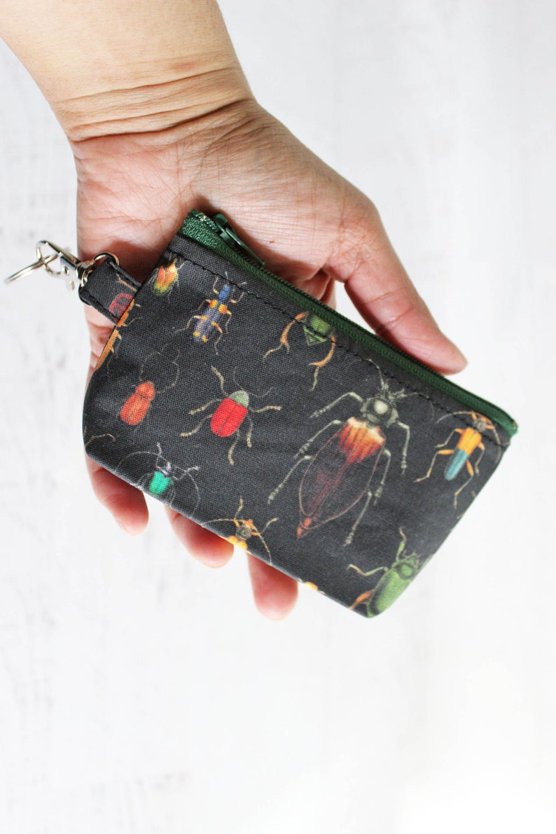 May include: A small black zippered pouch with a key ring. The pouch is covered in a pattern of colorful beetles.