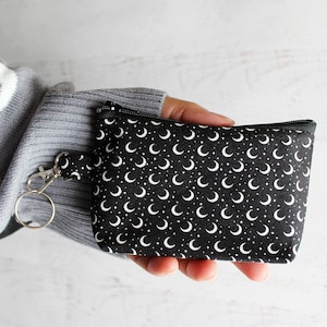 May include: A small black zippered pouch with a white crescent moon and star pattern. The pouch has a silver key ring attached.