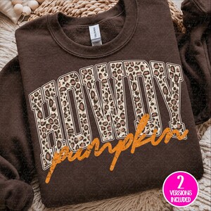 Puede incluir: Una sudadera de cuello redondo color marr&oacute;n oscuro con la palabra HOWDY en letras grandes de estilo bloque con un patr&oacute;n de leopardo beige y marr&oacute;n. Debajo de la palabra HOWDY, la palabra pumpkin est&aacute; escrita en cursiva naranja desgastada.