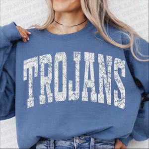May include: A light blue sweatshirt with the word "TROJANS" printed in distressed white lettering. The sweatshirt is a solid color and has a crew neck. The image is a close-up of the upper body.